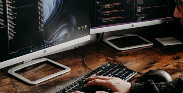 Desenvolvedor programando com dois monitores em ambiente com mesa de madeira